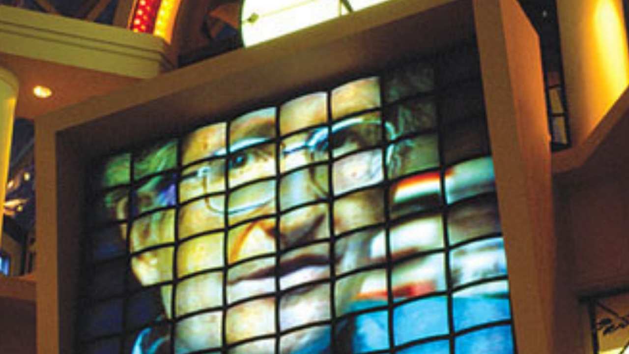 man with glasses on tv screens